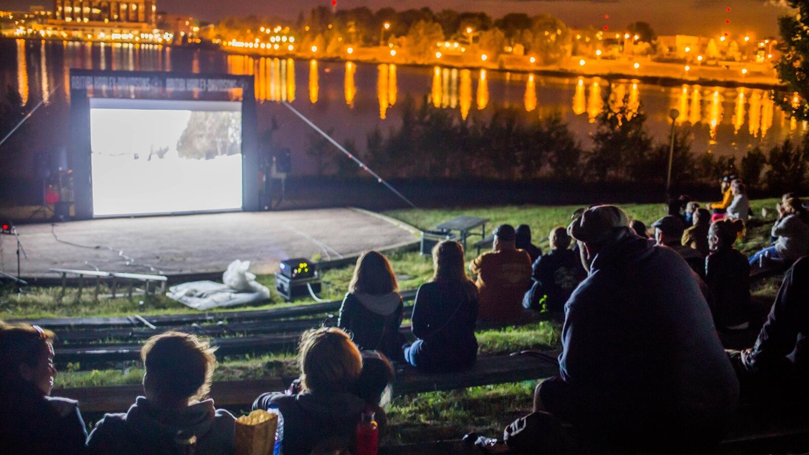 Des gens assistent à une projection de film en plein air, la nuit.