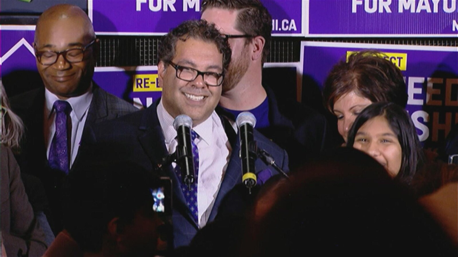 Naheed Nenshi souriant sur un podium, entouré de partisans