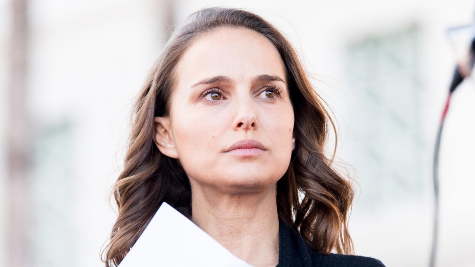 L'actrice Natalie Portman tient une feuille de papier à la main et regarde au loin.