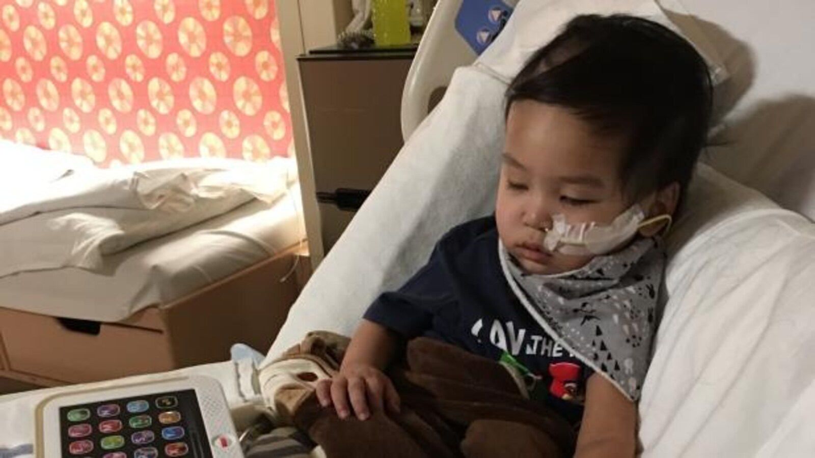Un bambin allongé sur un lit avec une sonde dans le nez.