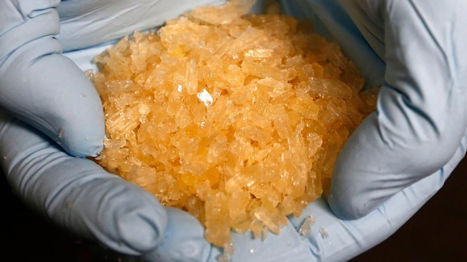 Quelqu'un portant des gants tient une quantité importante de cristaux orangés de méthamphétamine.