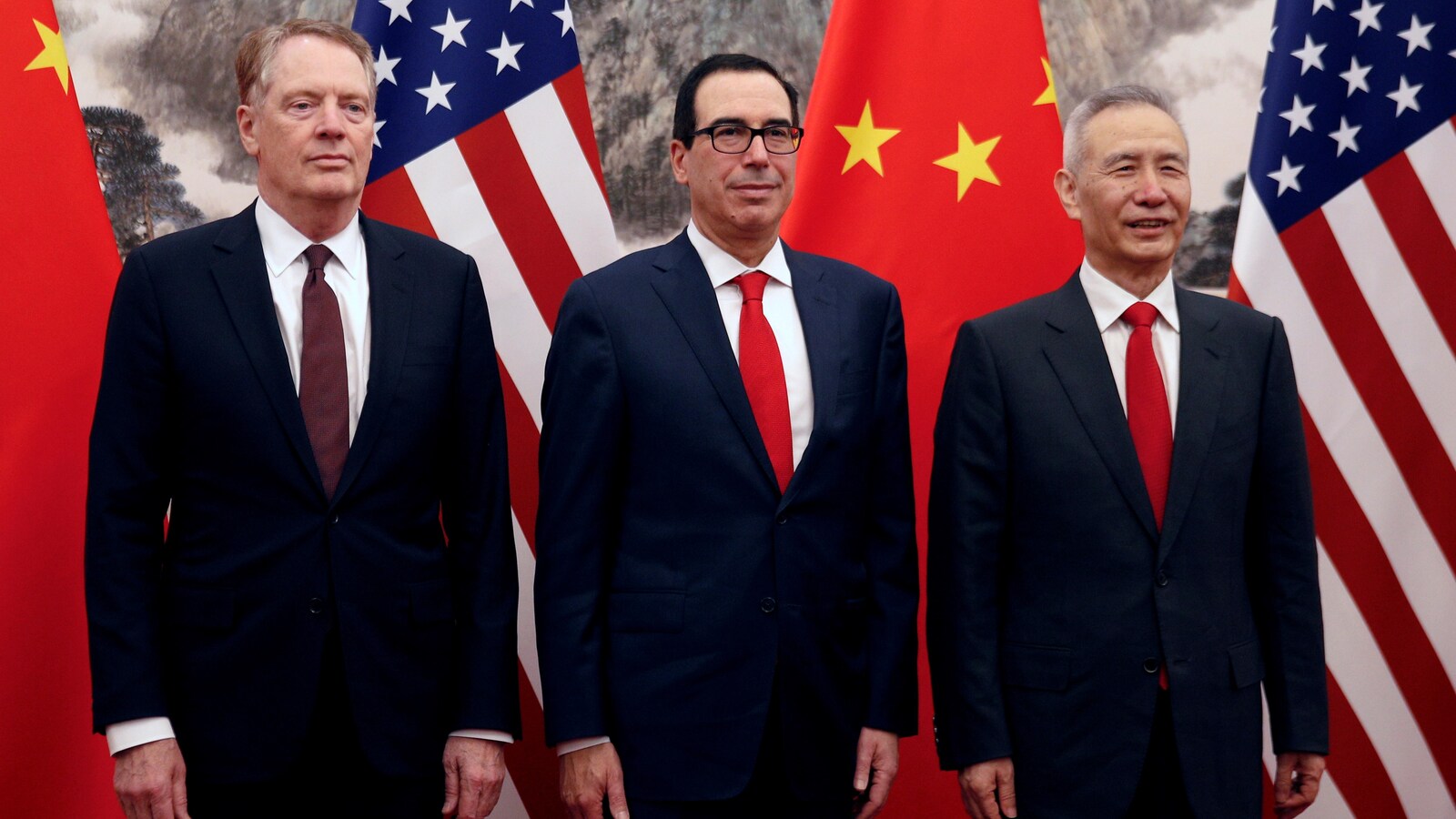 Trois hommes portant des vestons de couleur bleu marin et des cravates rouges posant devant les drapeaux américain et chinois.