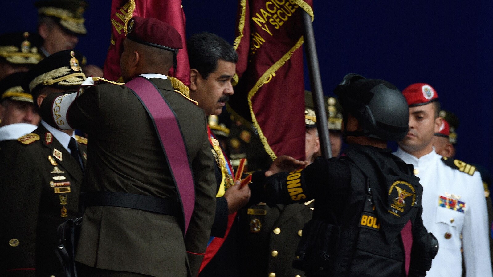 Un soldat habillé en noir entraîne le président Nicolas Maduro hors de l'estrade où il se tient,