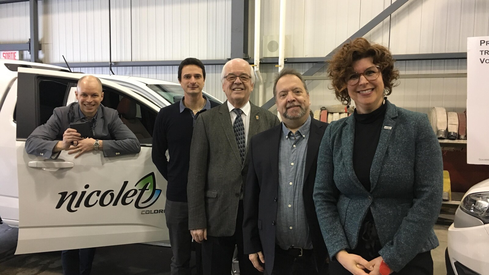 Cinq personnes posent devant une voiture électrique dans un garage.