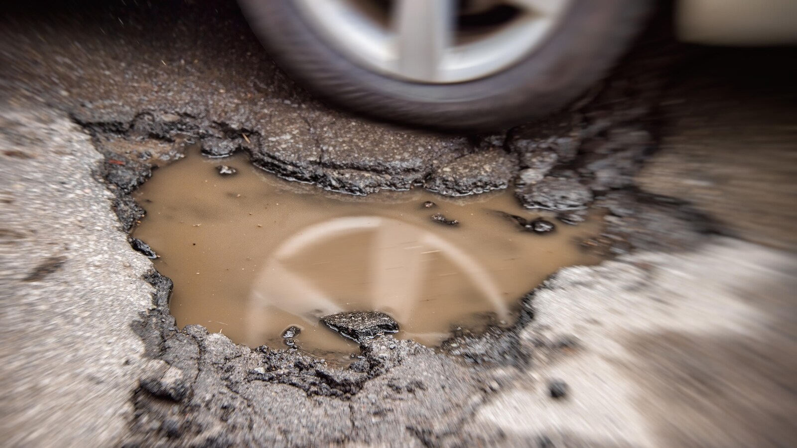 La roue d'une voiture passe près d'un nid-de-poule rempli d'eau boueuse.