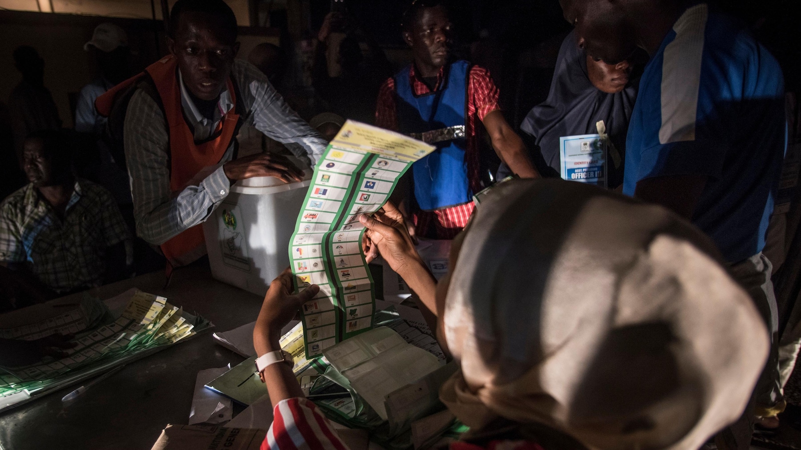 Une femme regarde un bulletin de vote alors que d'autres personnes s'affairent autour d'elle dans une pièce plongée dans la pénombre.