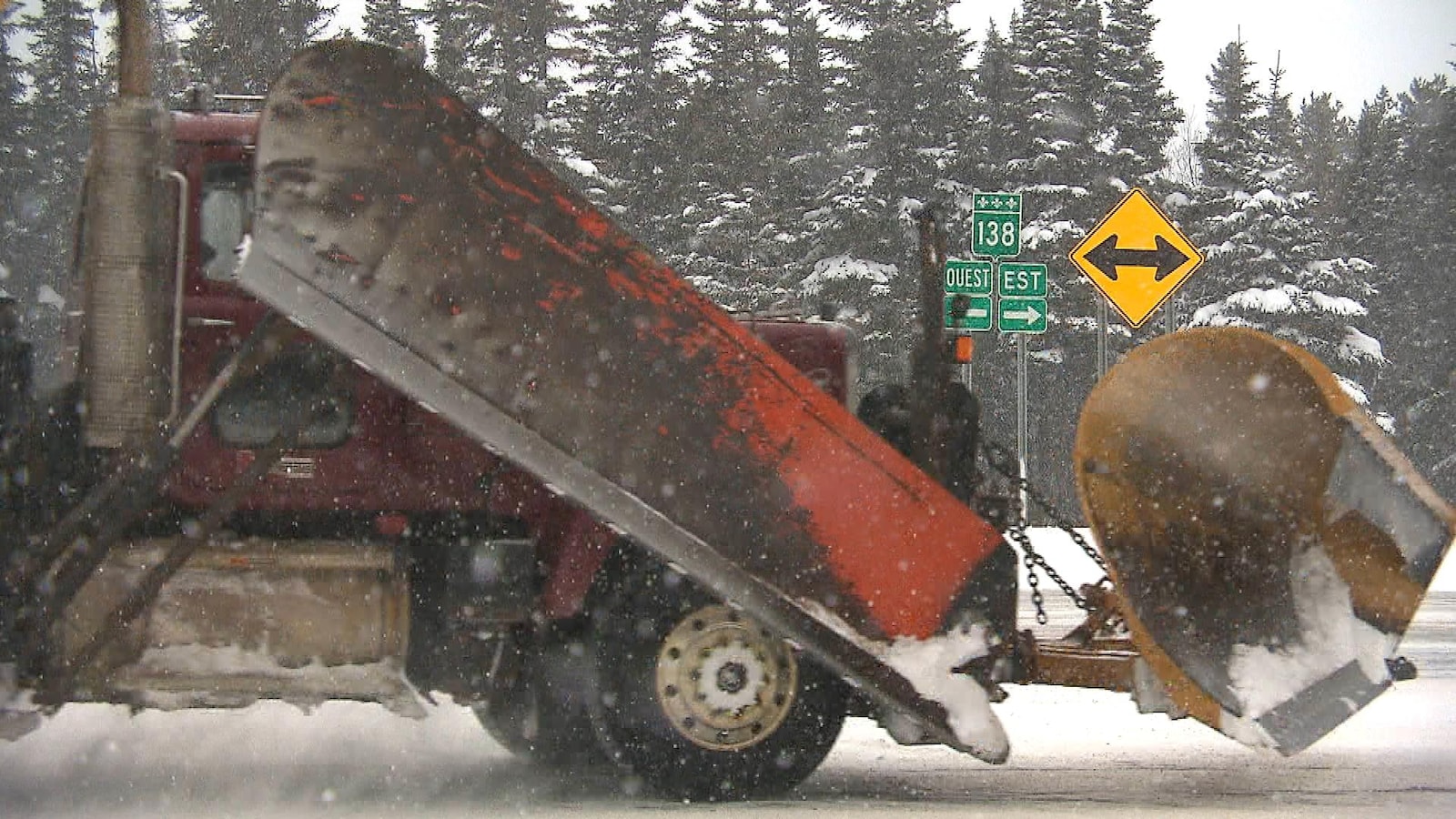 Un gros camion muni d'une niveleuse circule dans la neige sur la route 138