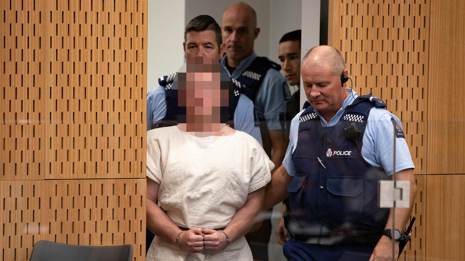 Un accusé vêtu d'une tunique est accompagné par des policiers.