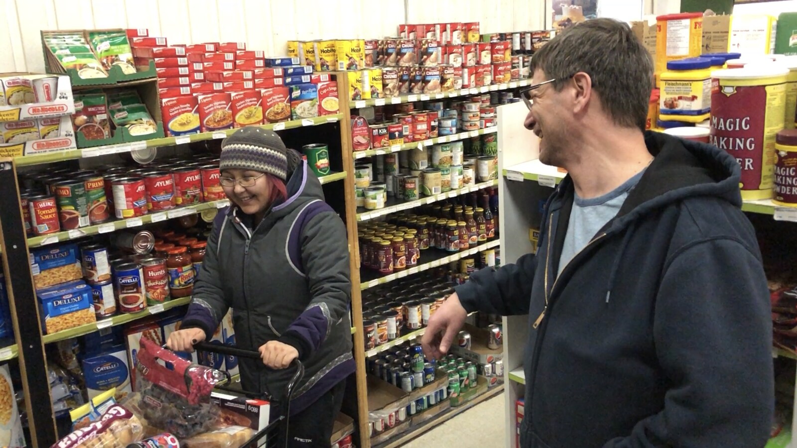 Un homme appuyé sur les étagères d'une épicerie sourit à une cliente.
