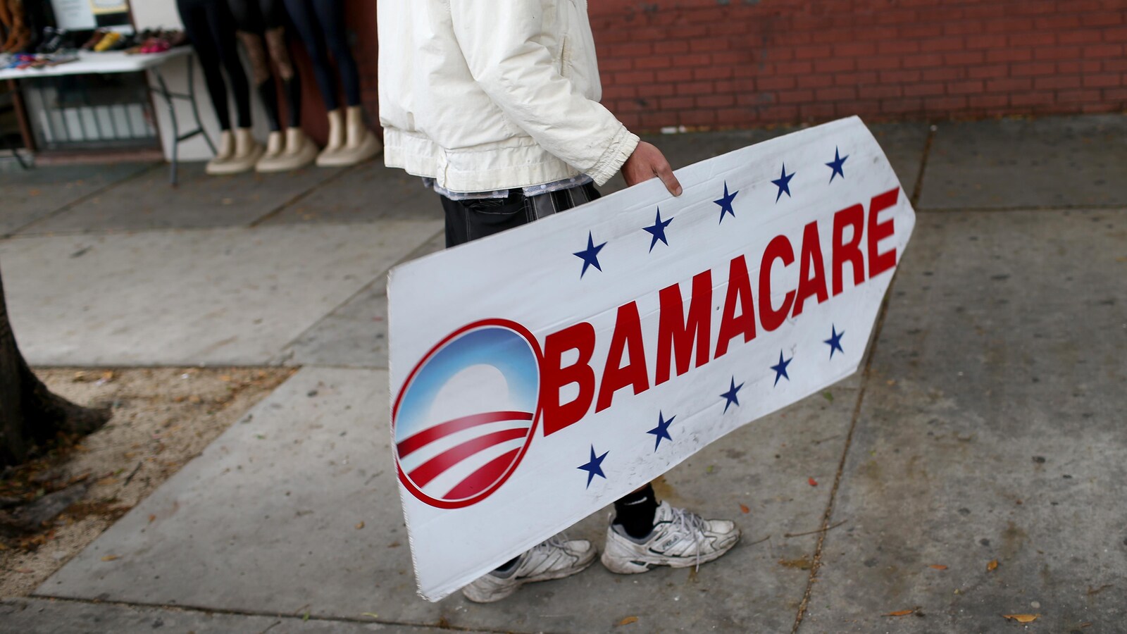 Une personne tient une affiche en forme de flèche sur laquelle il est écrit «Obamacare».