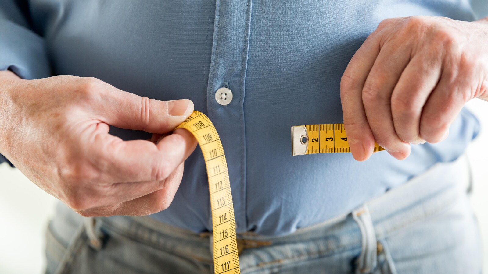 Gros plan sur les mains d'un homme qui mesure son tour de taille avec un ruban à mesurer.