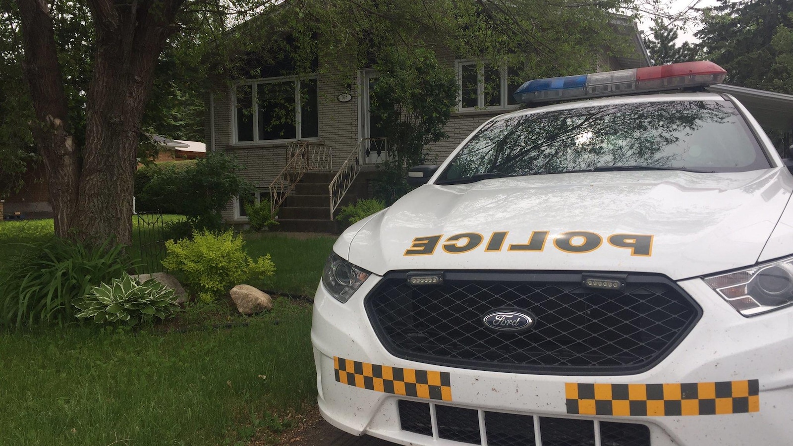 Une voiture de la Sûreté du Québec devant une résidence perquisitionnée.