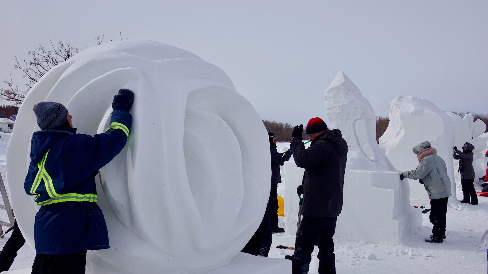 Des personnes taillent de la neige pour former des sculptures de neige à l'extérieur.