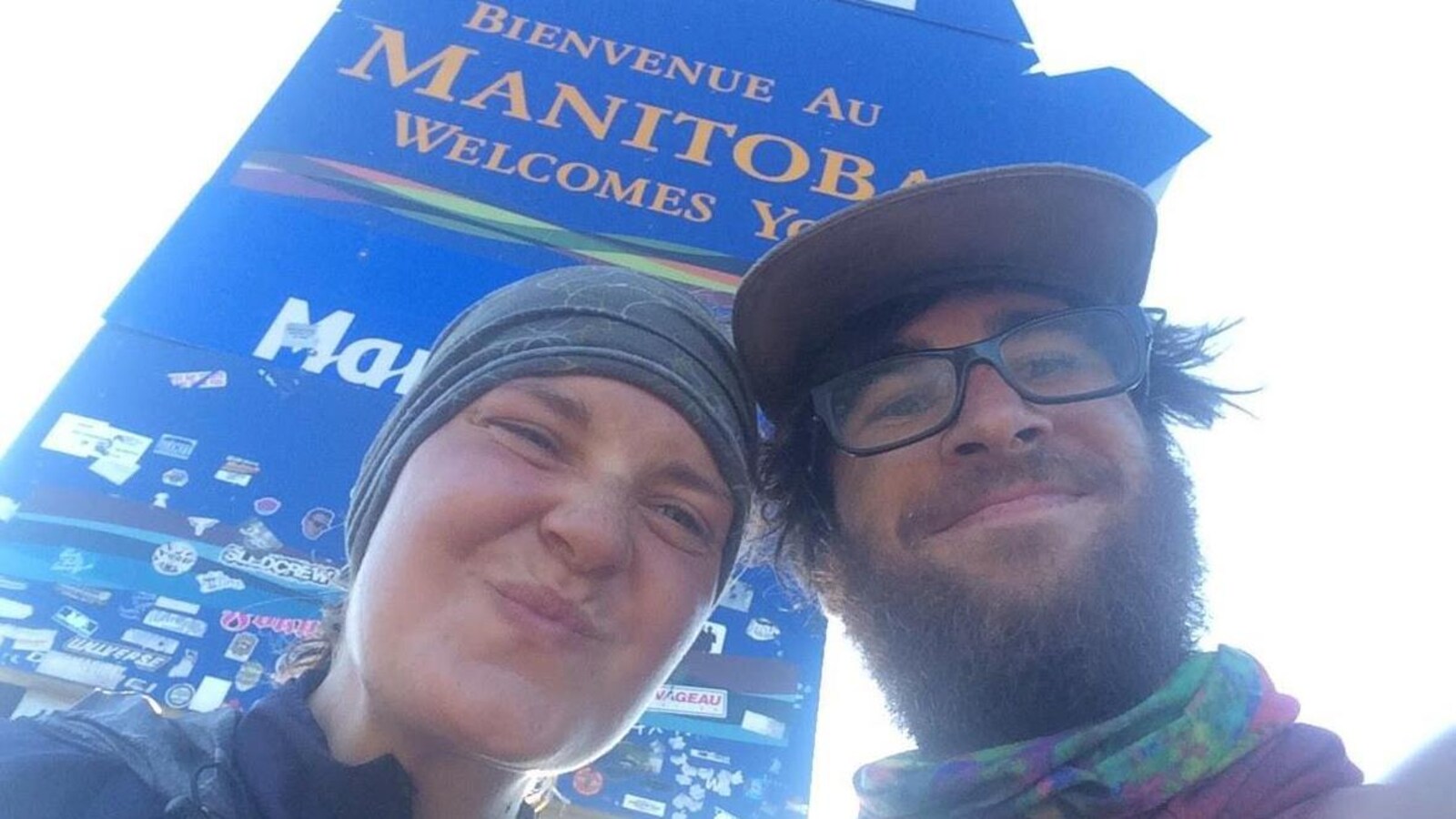 Un couple prend un égoportrait devant une pancarte indiquant: « Bienvenue au Manitoba ».