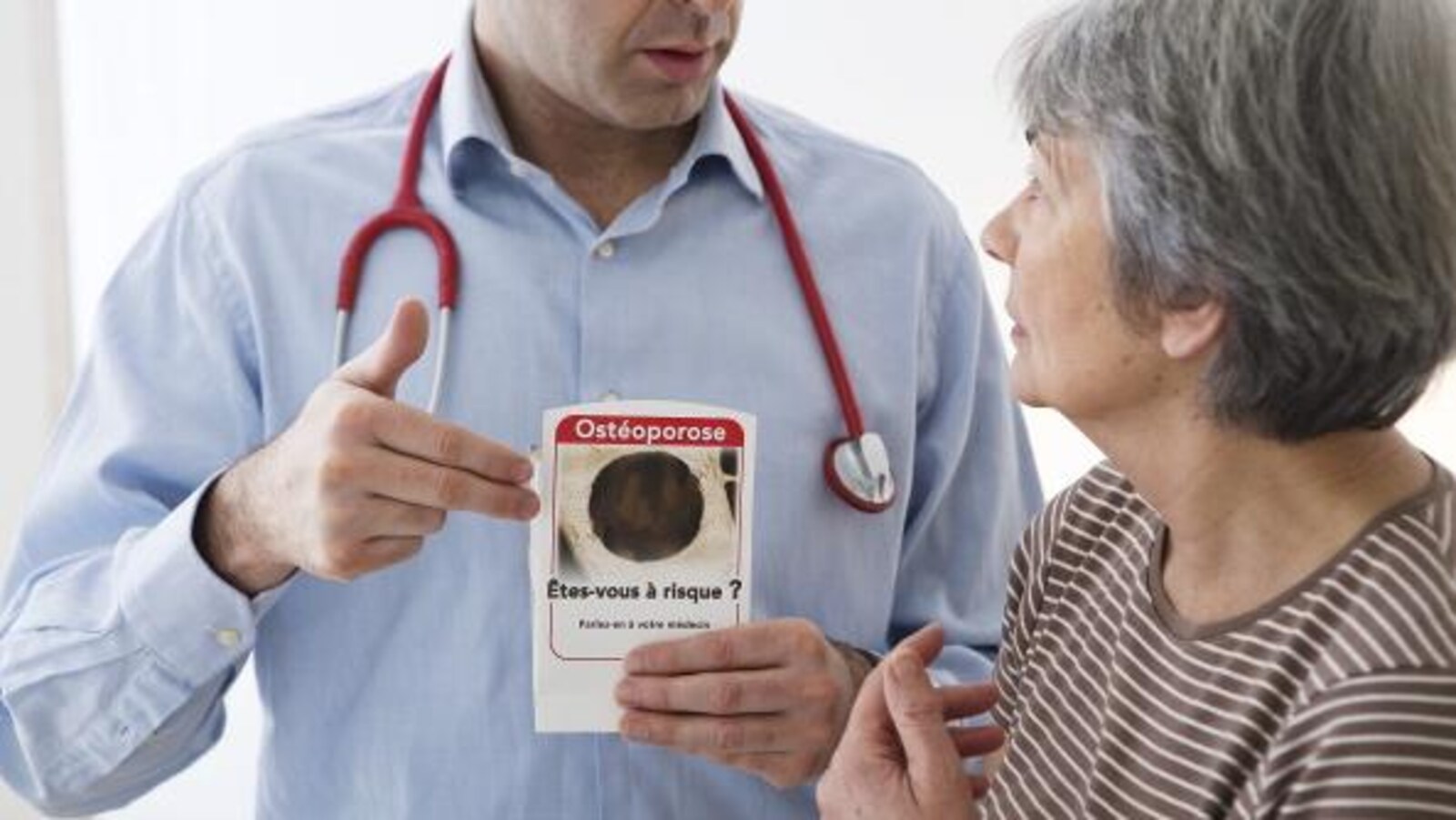 Un médecin parle à une patiente. Il tient une brochure qui dit : Ostéoporose, êtes-vous à risque?