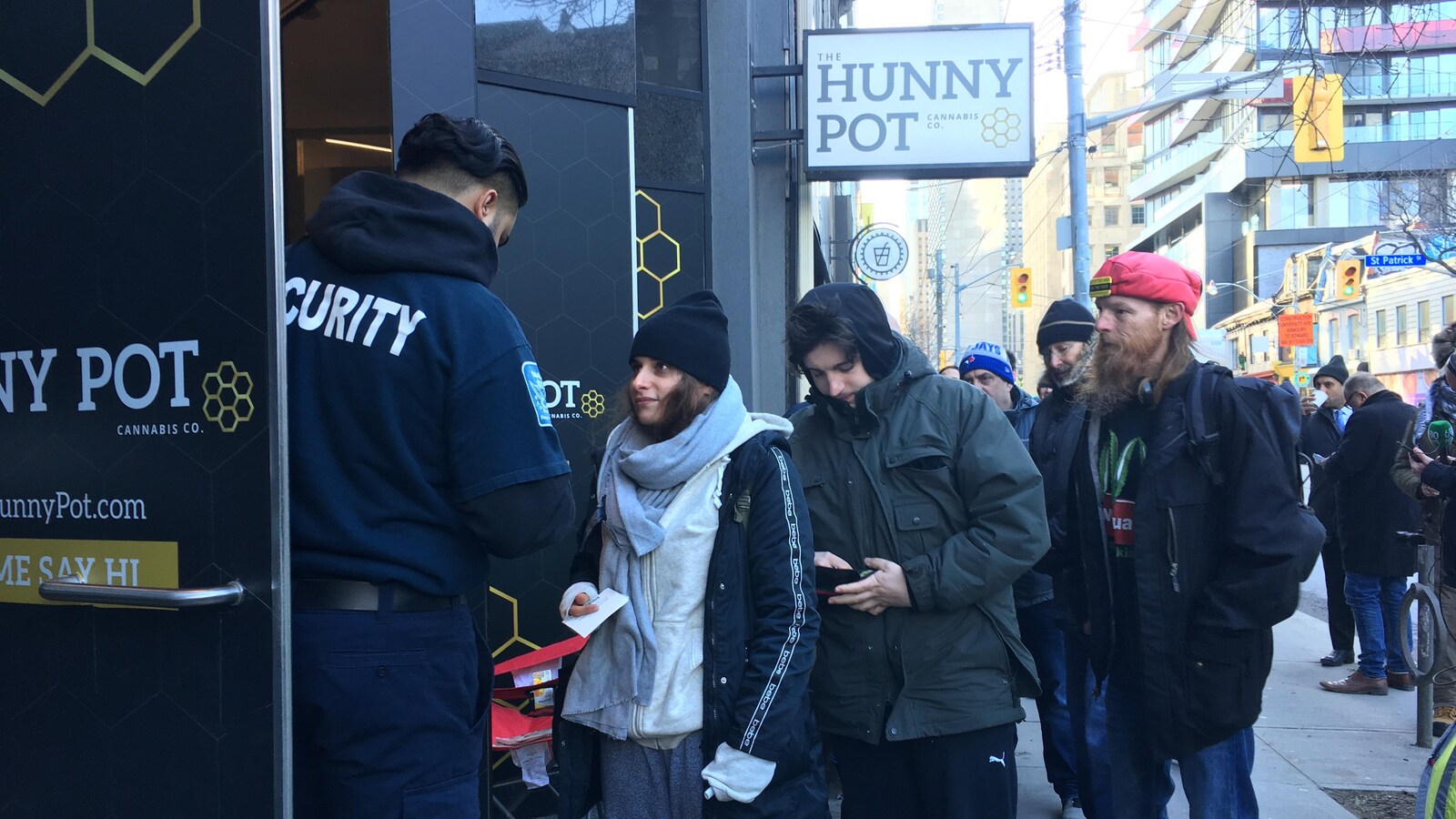 Photo de personnes en file sur le trottoir qui montrent leur carte d'identité à un agent de sécurité.