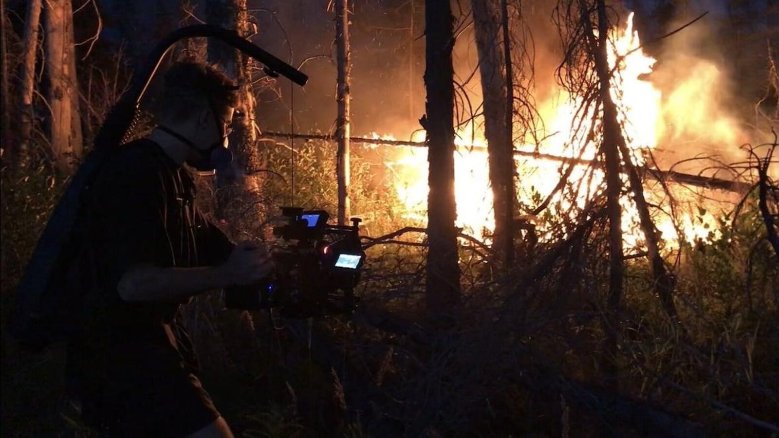 Un homme vu de côté qui filme un incendie de forêt.