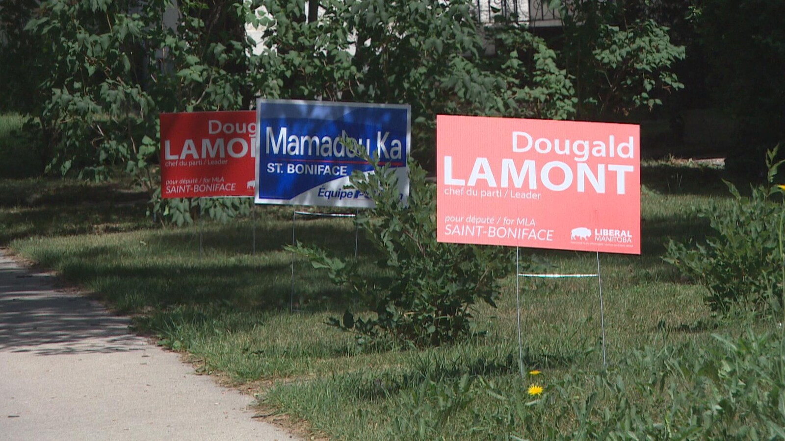 Deux pancartes rouges et une pancarte bleu sur une pelouse.