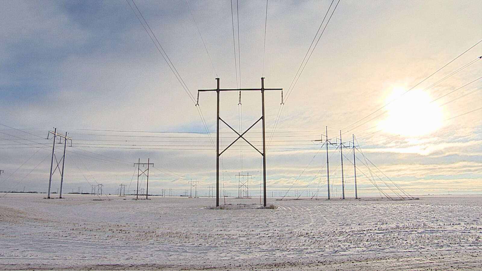 Hautes installations électriques dans un cmap avec de la neige et un ciel nuageux.