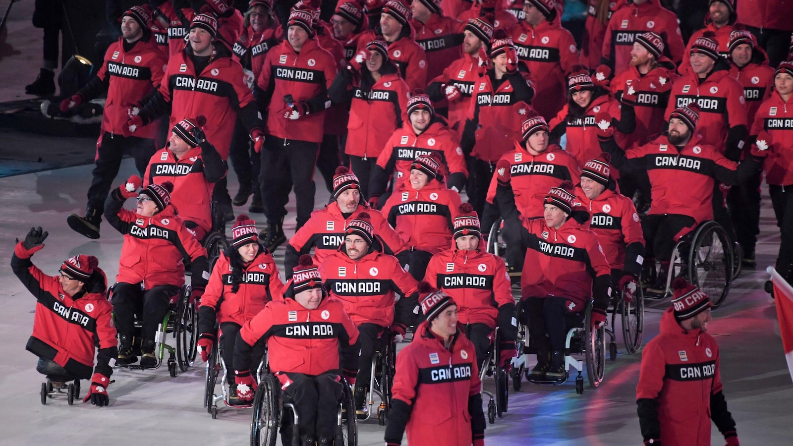 Des athlètes canadiens marchent et saluent la foule.