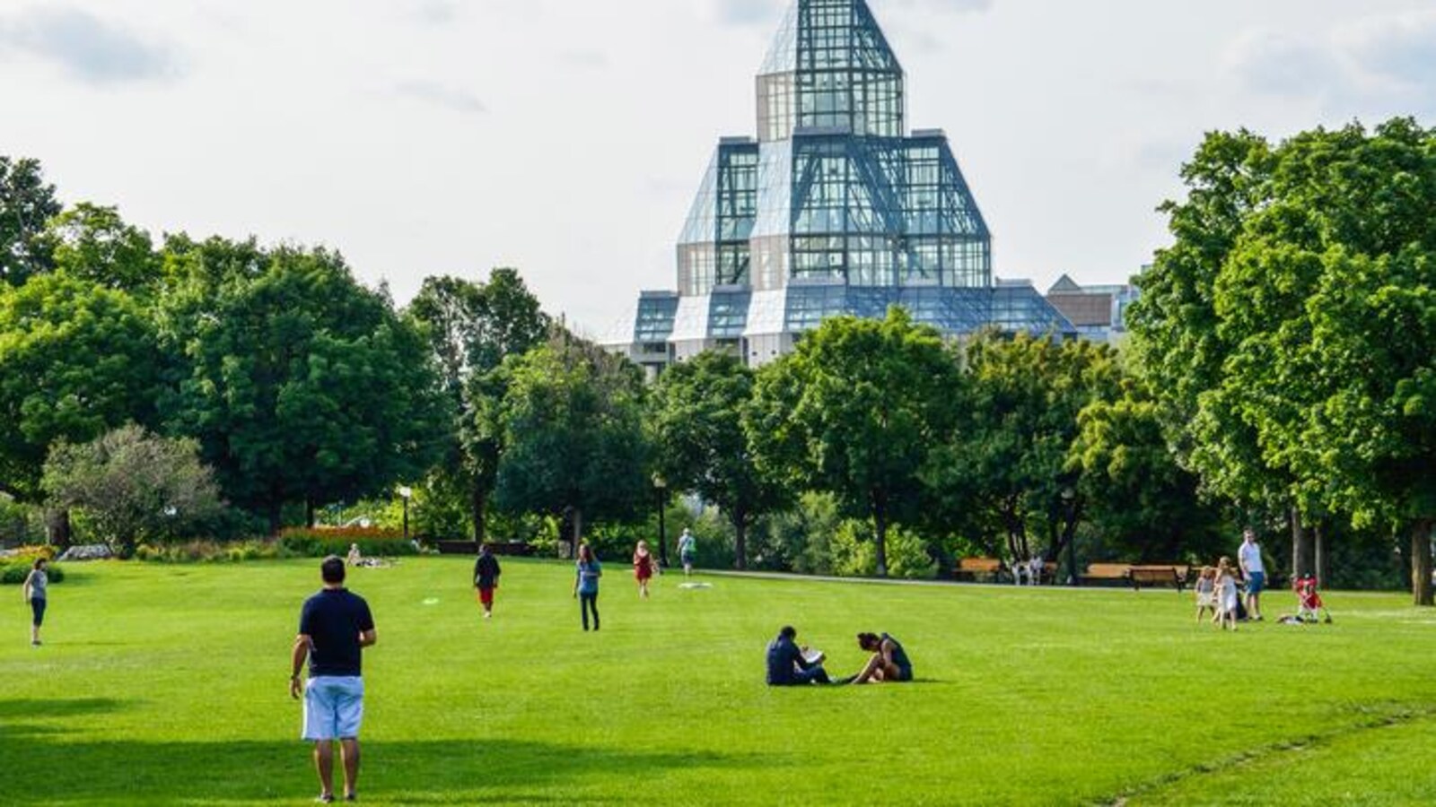 Des gens qui marchent et des gens qui sont assis sur le gazon devant le Musée des beaux-arts du Canada.