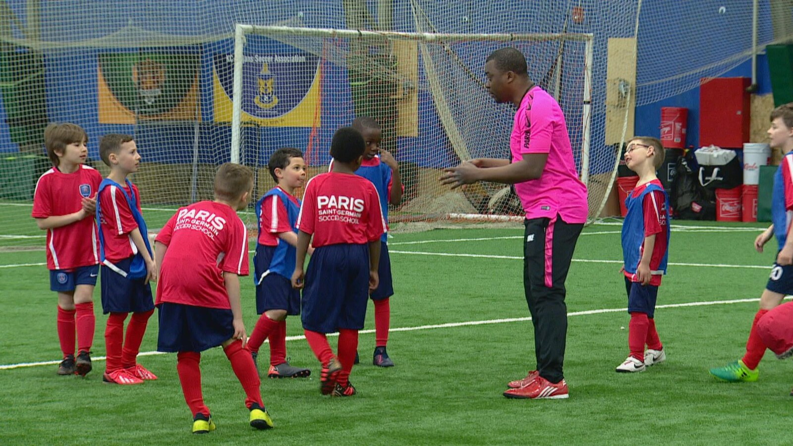 Des enfants en maillot de soccer écoute leur entraîneur sur un terrain.
