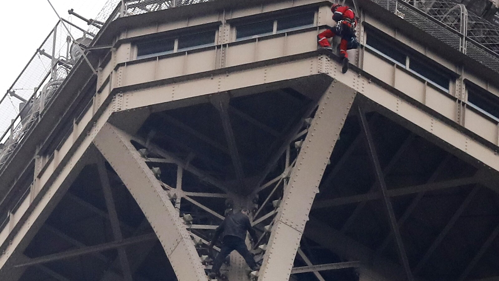 Un homme en noir se tient aux barreaux de la tour Eiffel.
