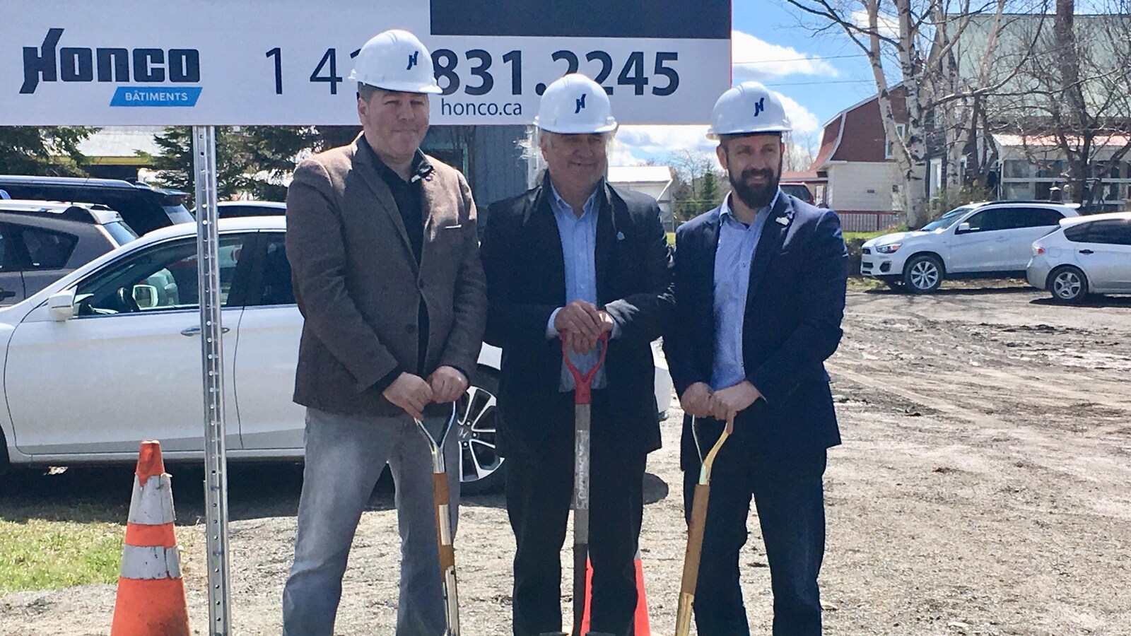 Trois hommes souriants portant un casque de construction sur la tête tiennent chacun une pelle.