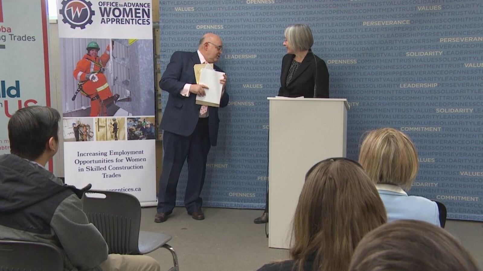 Un homme regarde vers les fesses d'une femme qui est derrière un podium.