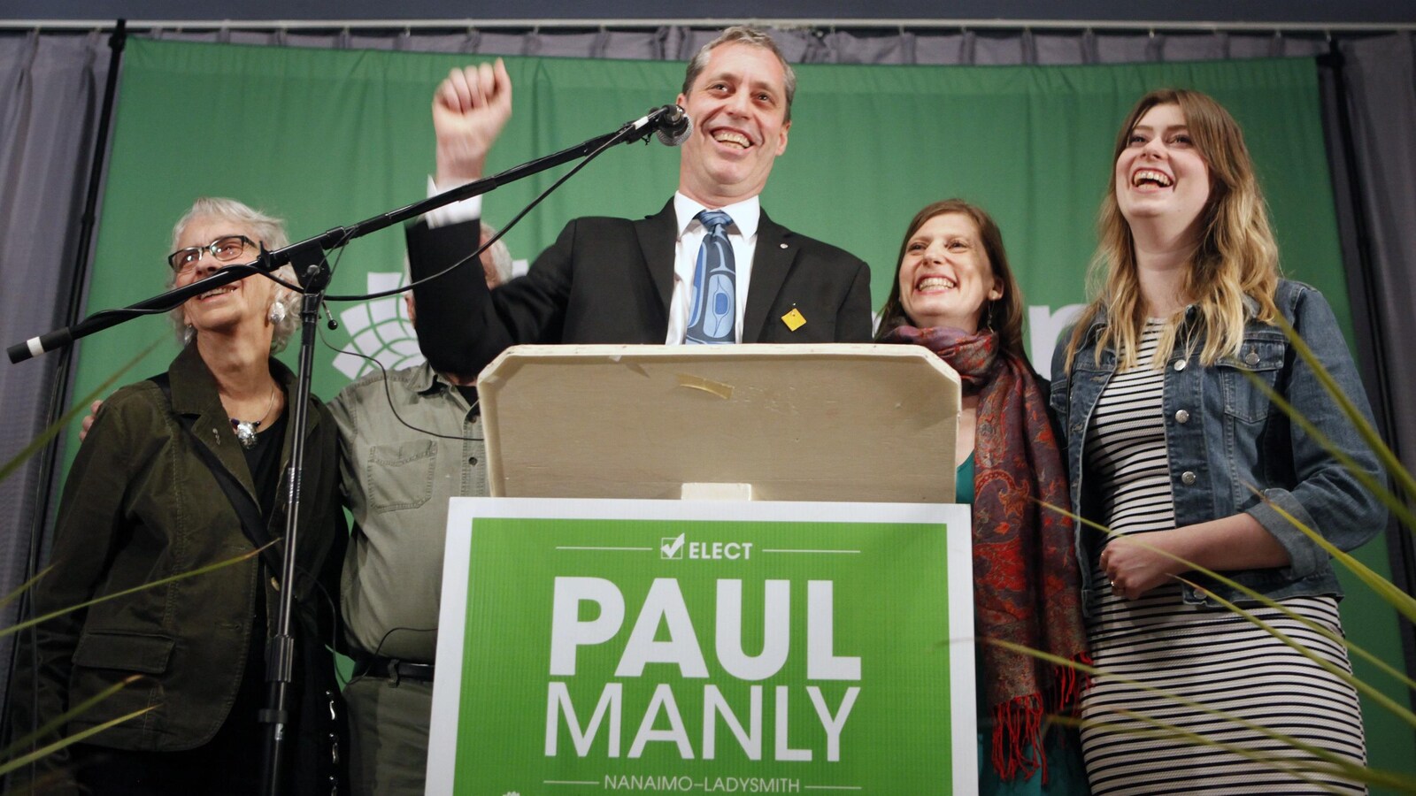 Accompagné de membres de sa famille, Paul Manly s'adresse au micro, le sourire aux lèvres et le poing levé en signe de victoire.