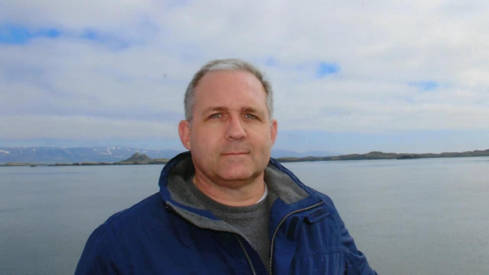 Paul Whelan, devant une étendue d'eau, regarde la caméra.