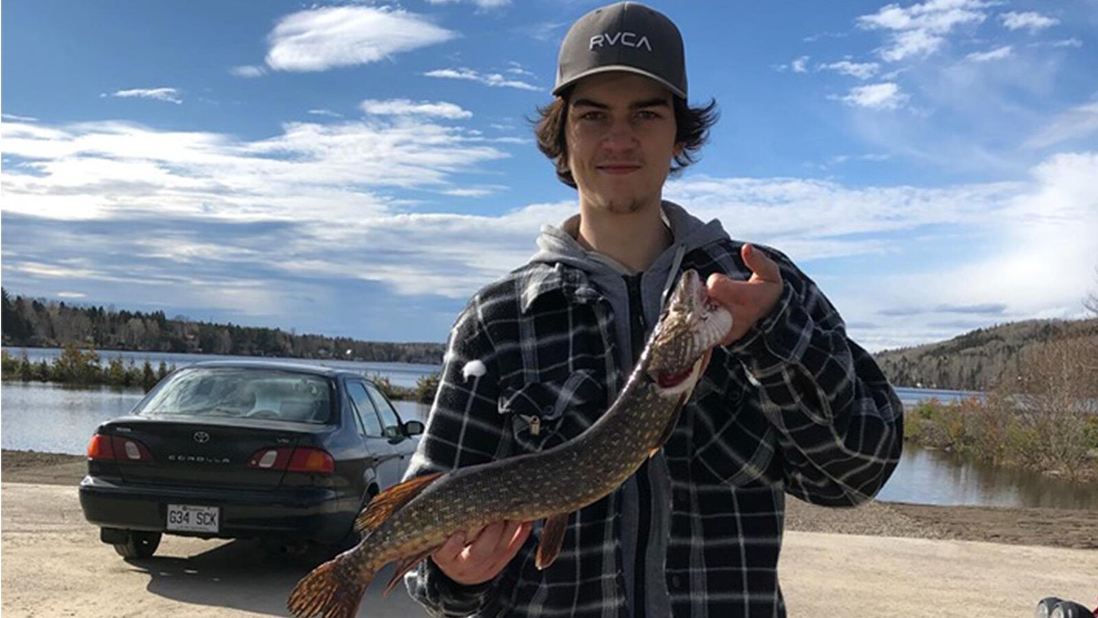 Un jeune homme prend la pause avec un brochet dans les mains.