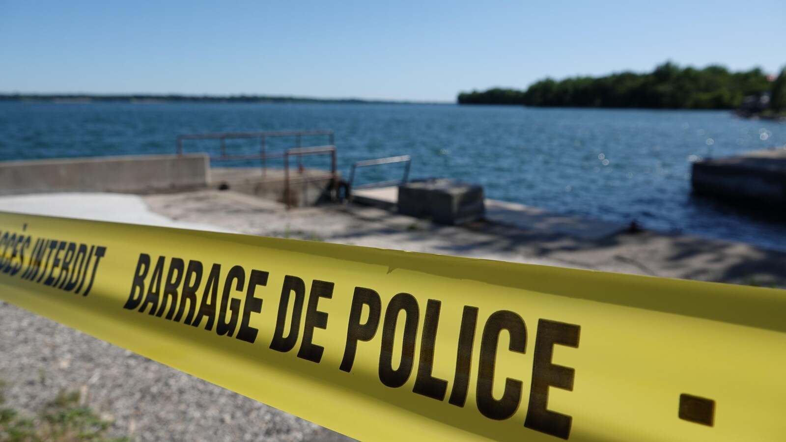 Un ruban sur lequel on peut lire « Barrage de police » est vu près d'une rive, lors d'une journée ensoleillée.