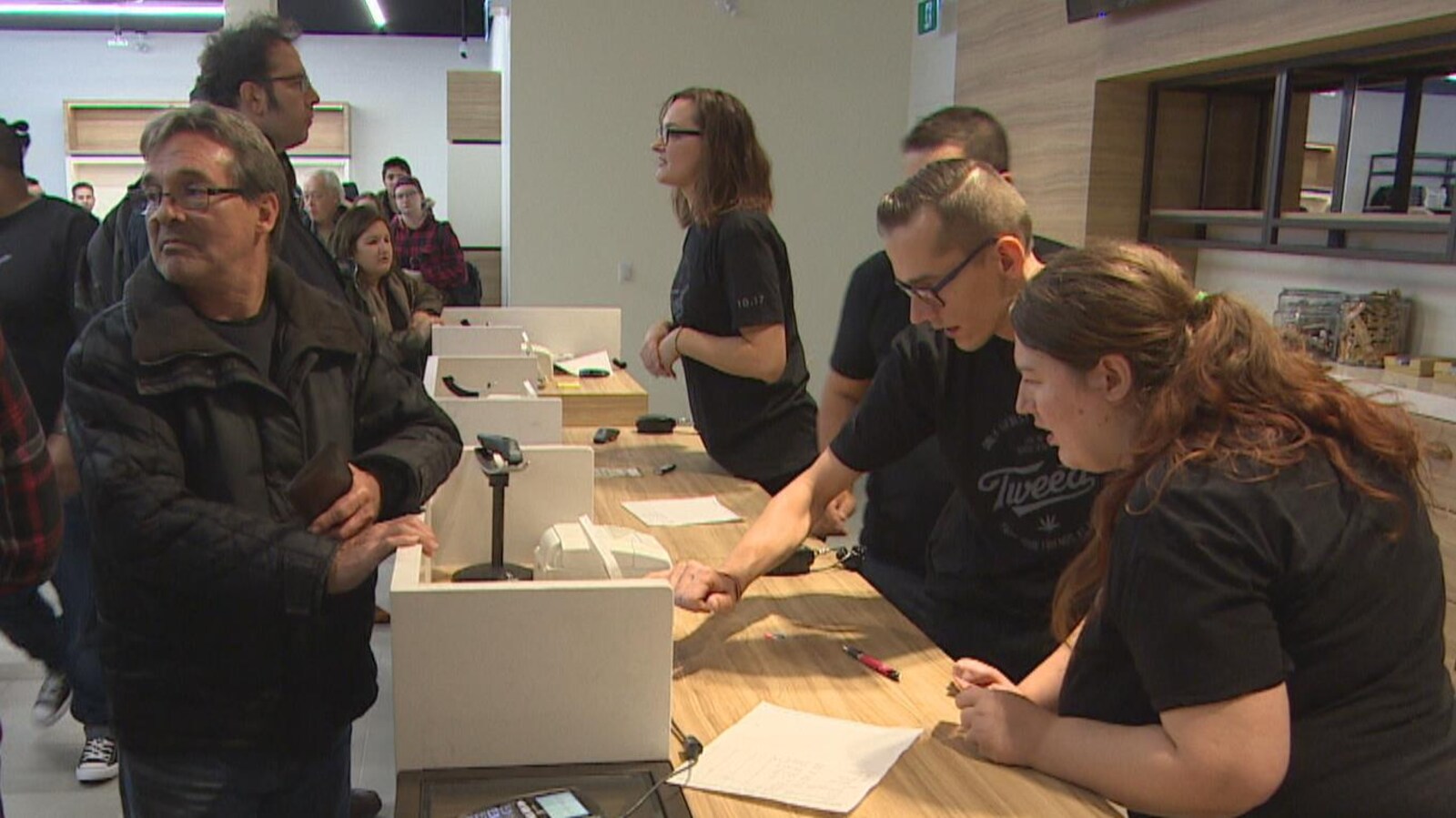 Au comptoir en bois clair d'un magasin de cannabis, les clients attendent pendant que les vendeurs s'empressent d'encaisser les ventes.