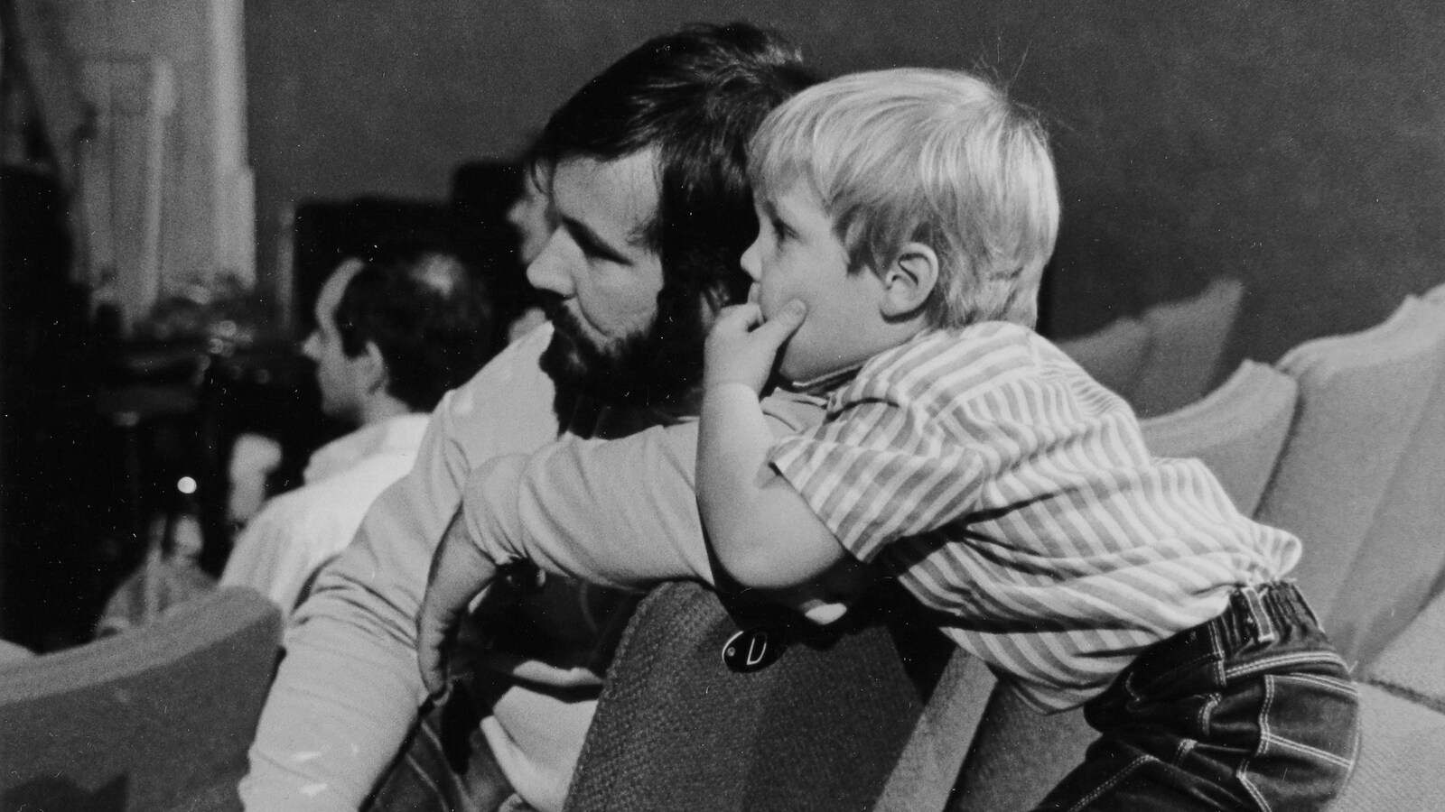 Un père et son fils tournés vers la scène d'un amphithéâtre, le fils appuyé sur l'épaule du père.