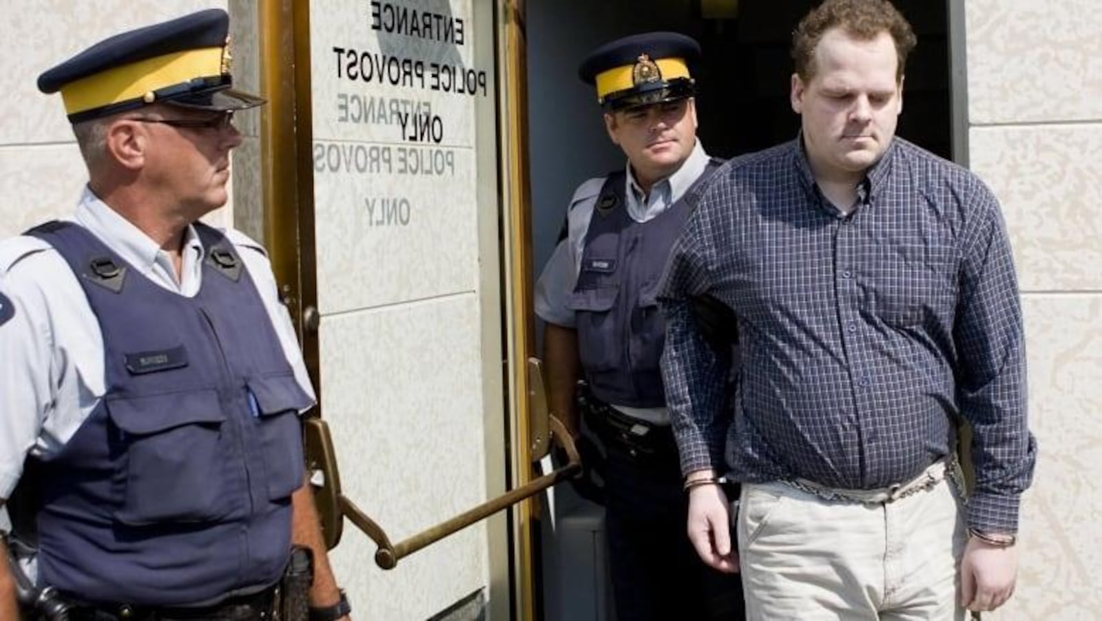 Peter Whitmore menotté est accompagné par deux agents de police.