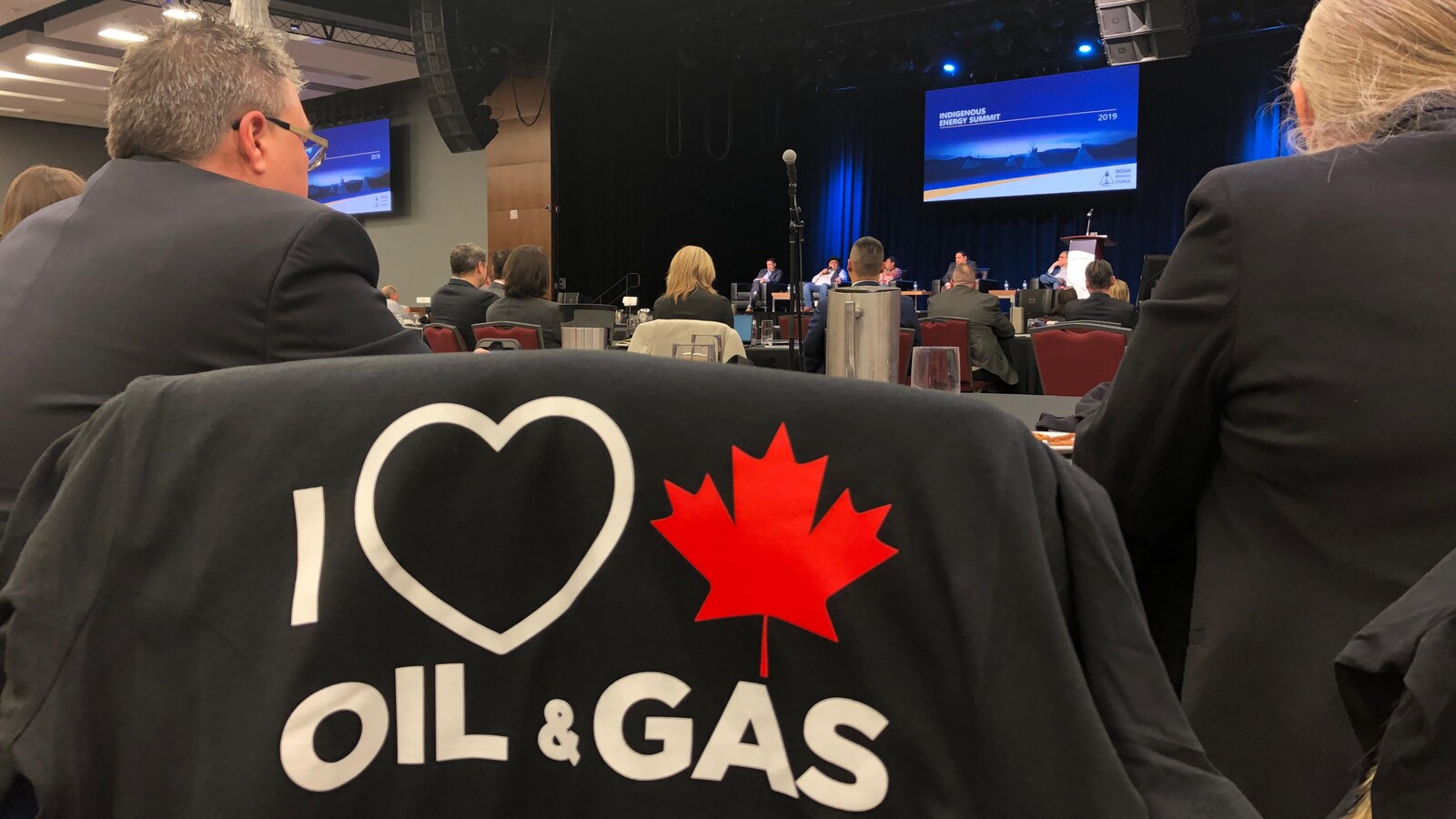 Des participants au Sommet autochtone sur l'énergie écoutent les membres d'un panel discuter sur scène des enjeux énergétiques.