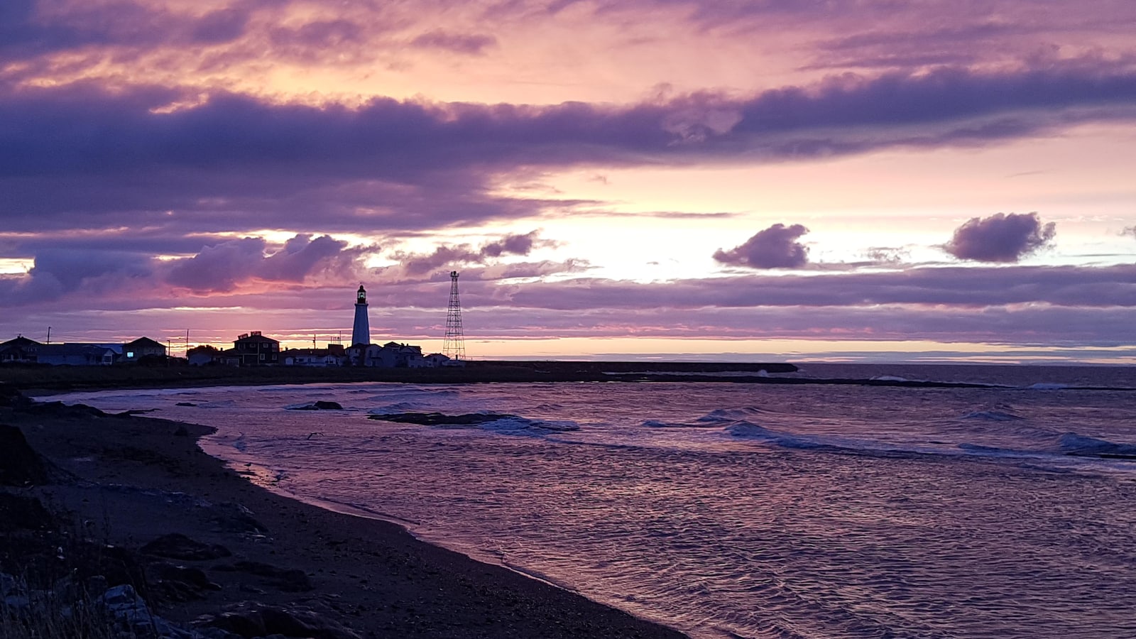 À l'avant-plan, on voit une berge et la mer ; au loin, le phare de Pointe-au-Père.