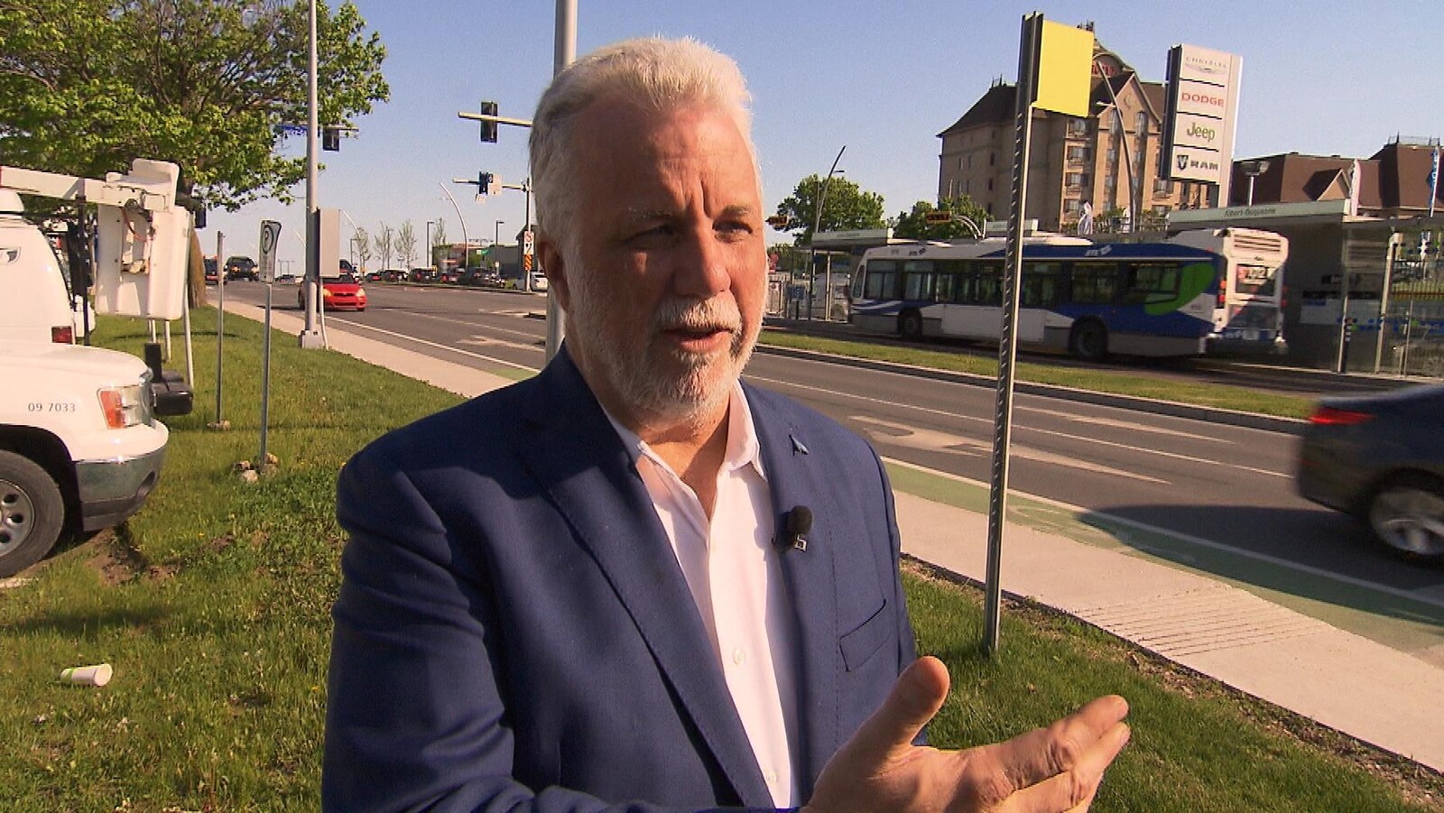 Le premier ministre du Québec, Philippe Couillard, en entrevue devant une rue passante. Un autobus est en arrière-plan.