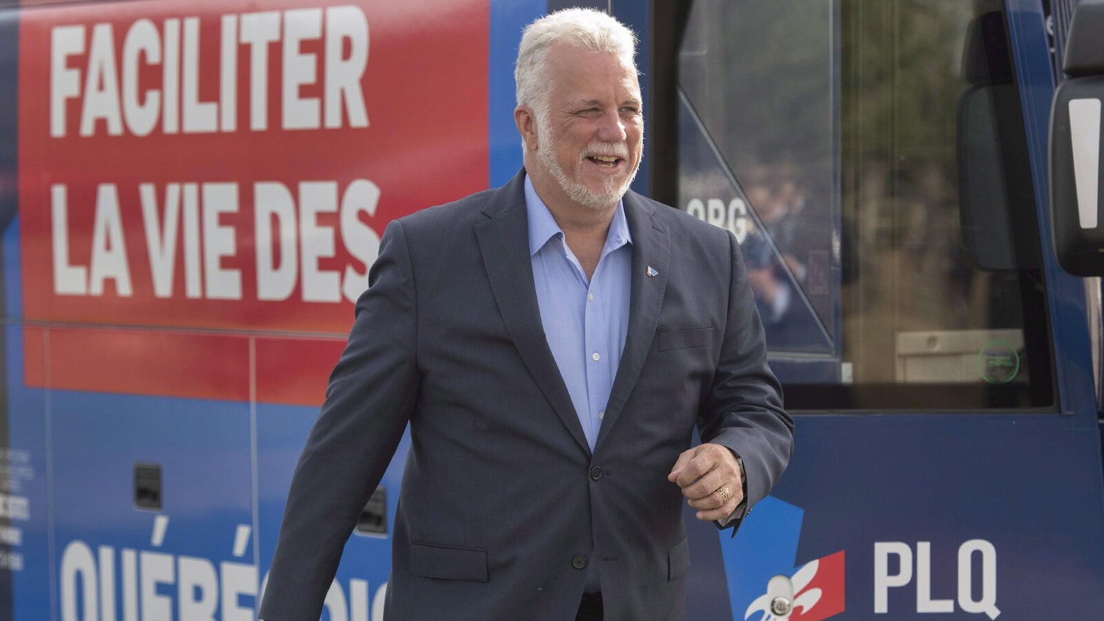 Philippe Couillard, devant son autobus de campagne, sur lequel on peut lire le slogan électoral du Parti libéral, « Faciliter la vie des Québécois ».