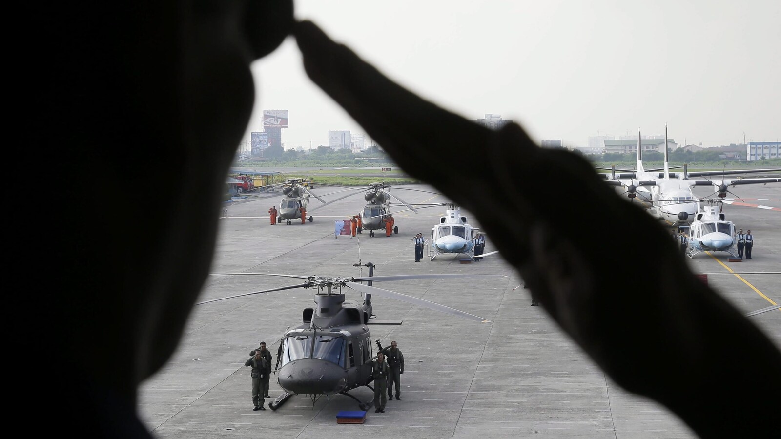 Des hélicoptères stationnés sur un tarmac sont visibles derrière la silhouette d'un militaire faisant un salut.