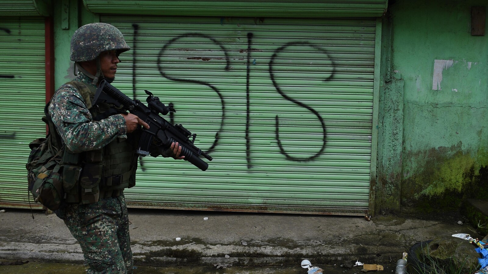 Un soldat philippin patrouille dans une rue de Marawi. Derrière lui, un graffiti sur une porte de garage écrit « ISIS », l'acronyme anglophone du groupe armé État islamique.