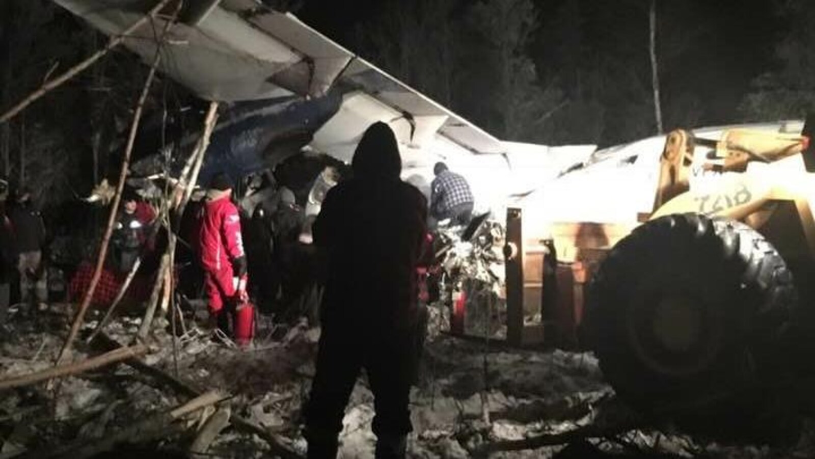 Un avion écrasé au sol, des gens s'activent dans le noir.