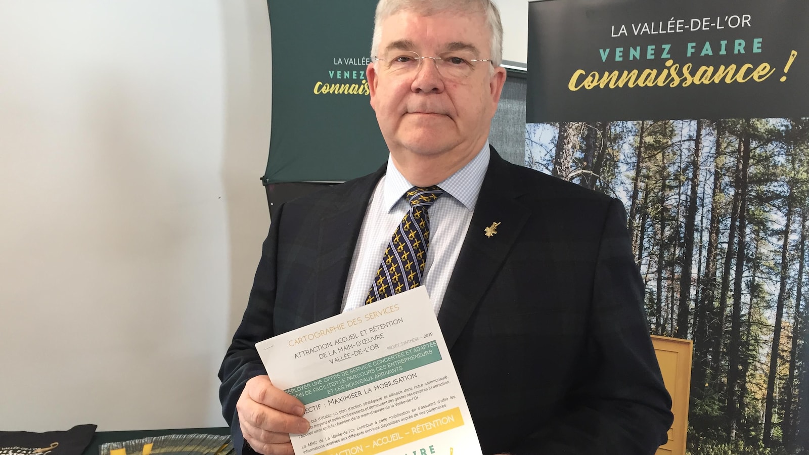 Pierre Corbeil tient un document, entouré de matériel promotionnel «La Vallée-de-l'Or, venez faire connaissance».