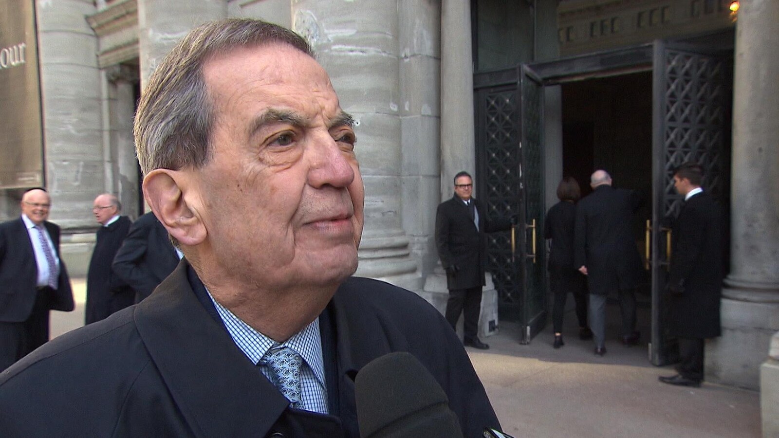 Pierre De Bané en entrevue, devant un grand bâtiment.