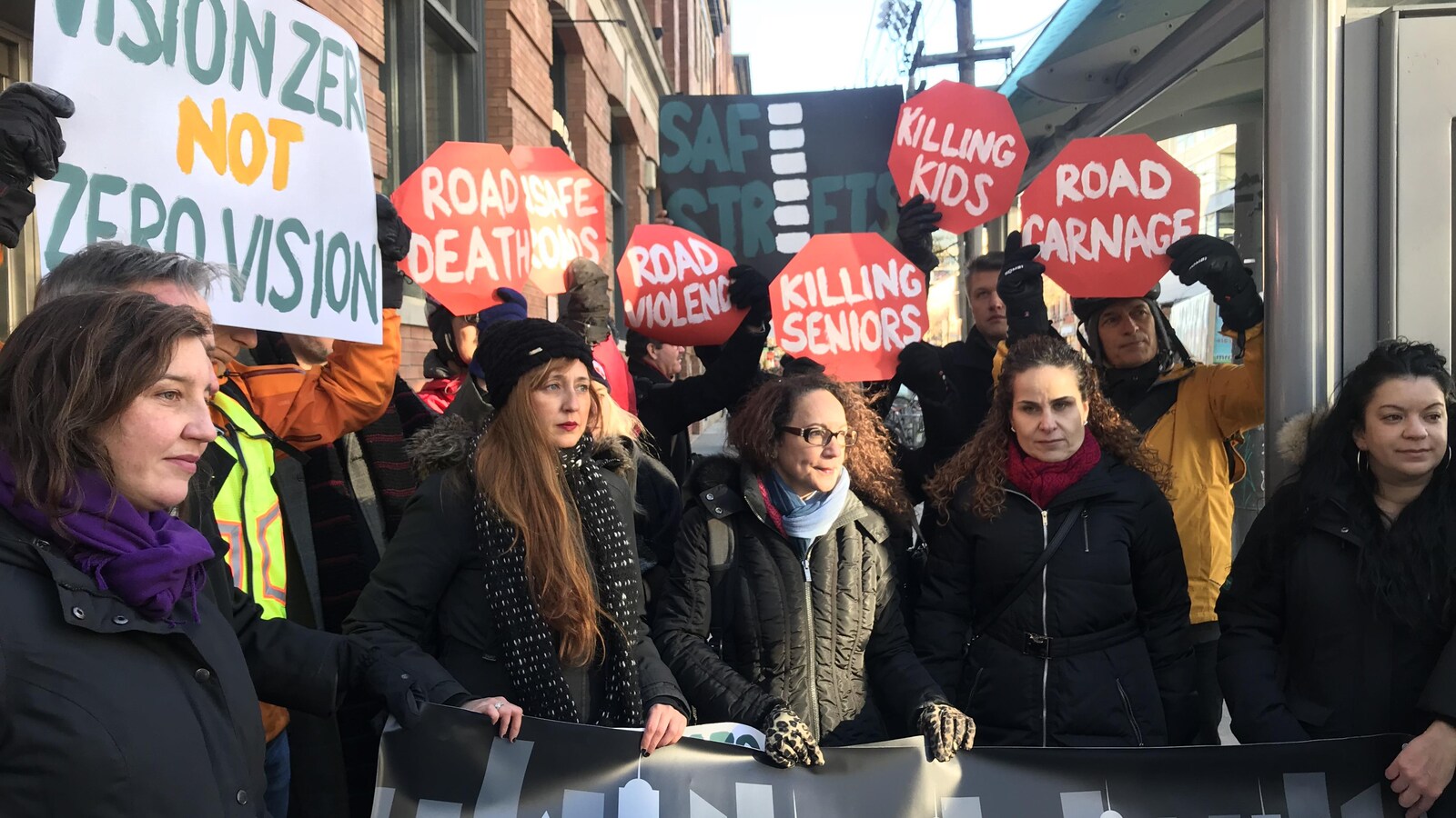 des groupes de défenseurs des piétons et des cyclistes brandissent des pancartes avec écrit : road carnage, killing kids, road death. il y a aussi la porte-parole du NPD Jessica Bell
