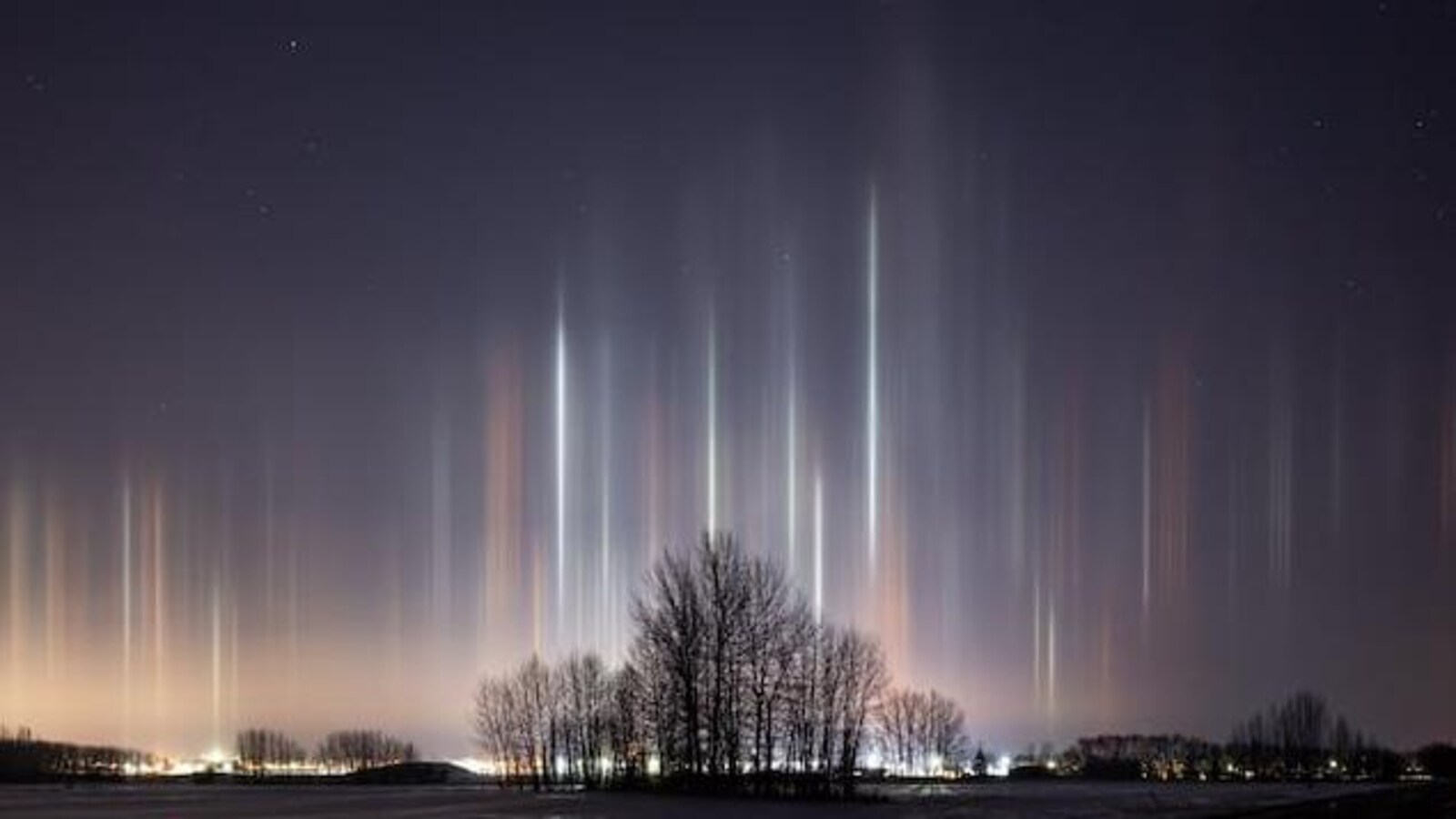 Une photo prise la nuit. Des faisceaux lumineux verticaux blancs et oranges semblent partir du sol pour s'élever dans les airs.