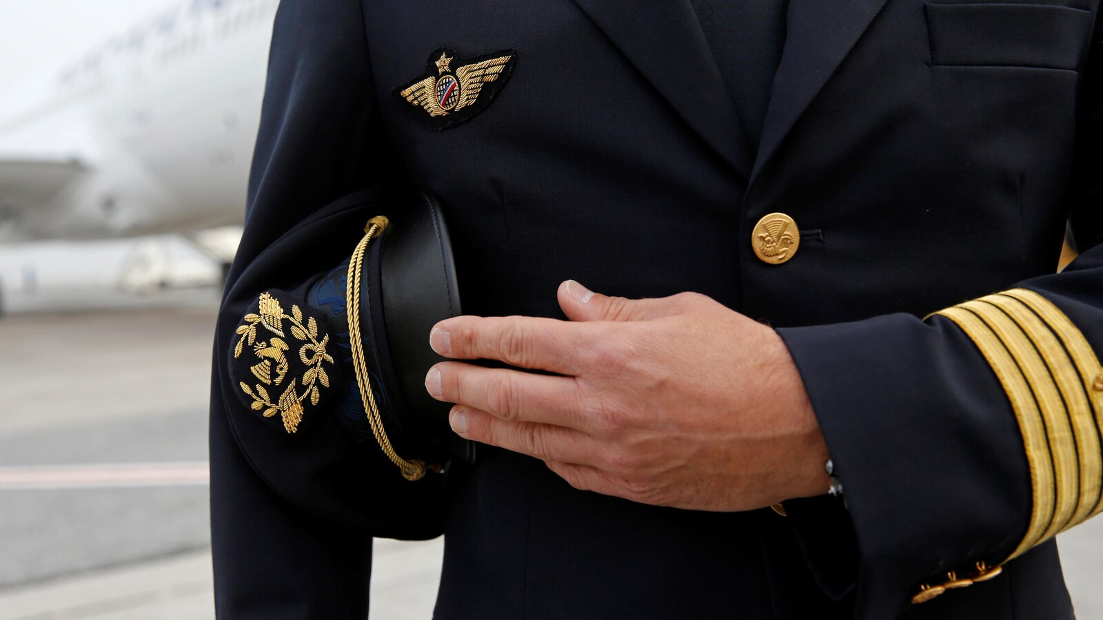 Un homme en tenue de pilote de l’aviation civile tient une casquette sous le bras.