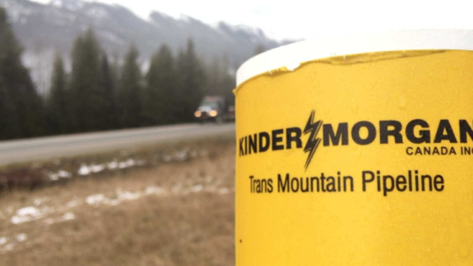 Logo de l'entreprise Kinder Morgan en premier plan, en bordure d'une route. L'entreprise Kinder Morgan affirme que l'attente des permis d'expansion du pipeline TransMountain, en Colombie-Britannique, a des répercussions coûteuses pour le projet.