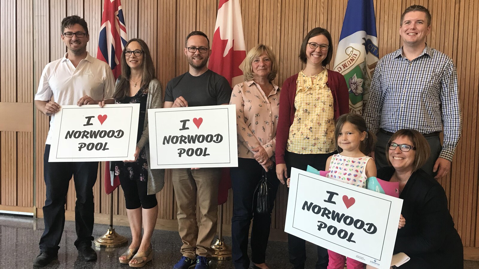 Plusieurs personnes posent pour une photo, en tenant des pancartes qui disent « I Love Norwood Pool ».